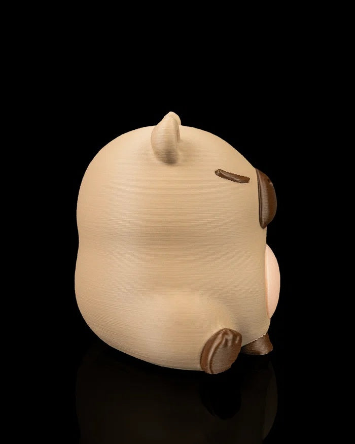 Side view of a capybara figurine showing its rounded seated body and dark foot detail.