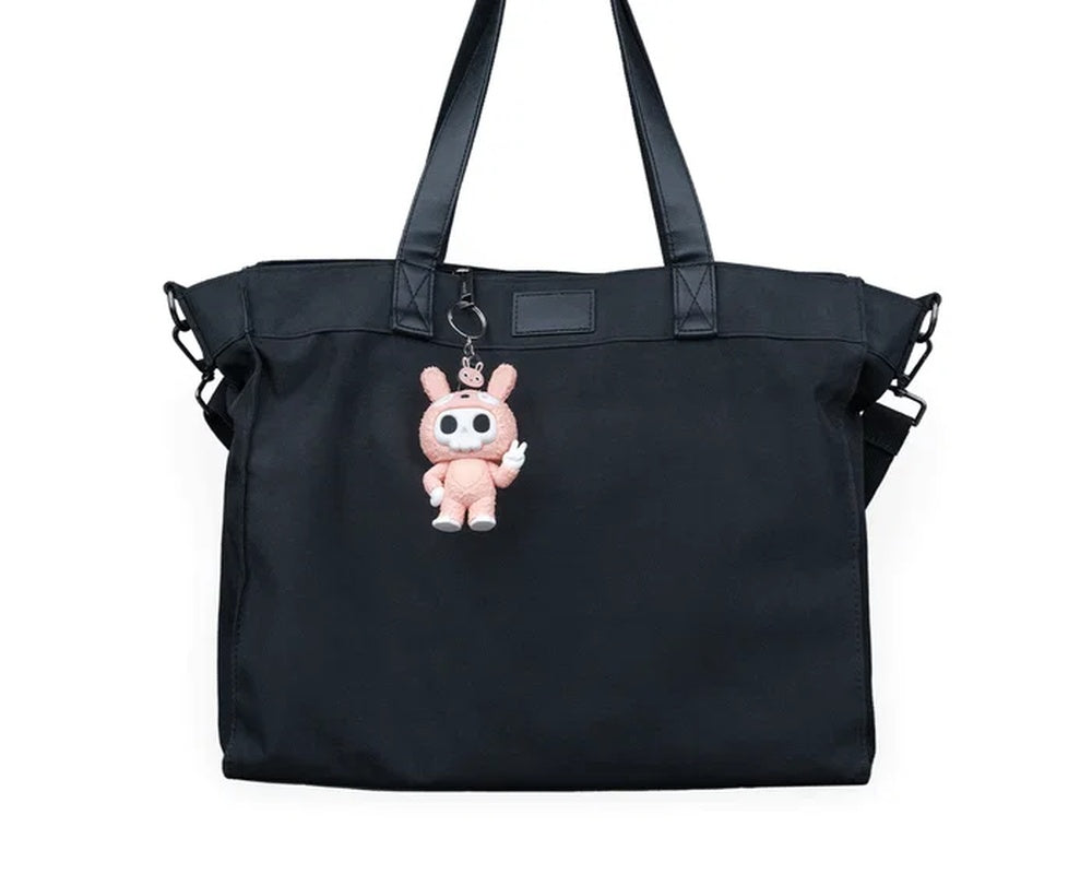 Small pink bunny-suit character hanging from a black bag by a metal ring